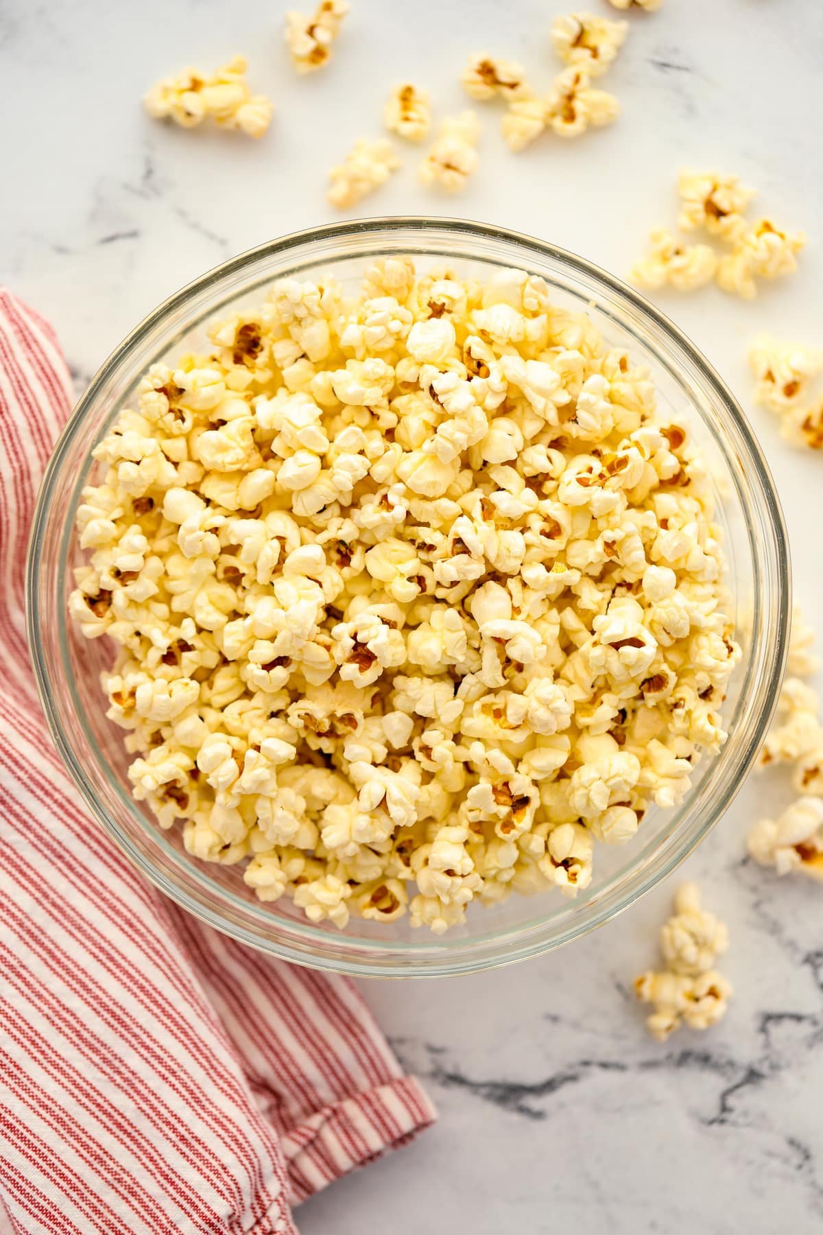 A large bowl of popcorn with a white and red napkin on the side.