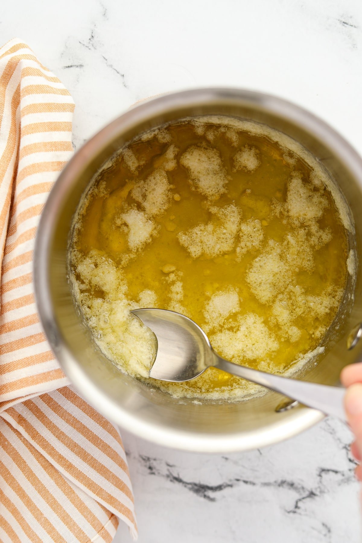 Using a spoon to remove foam from melted butter in a saucepan.