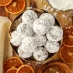 A bowl of chocolate truffles coated in powdered sugar, and surrounded by dried orange slices.