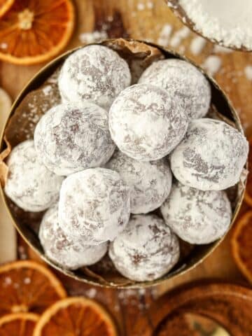 A bowl of chocolate truffles coated in powdered sugar, and surrounded by dried orange slices.