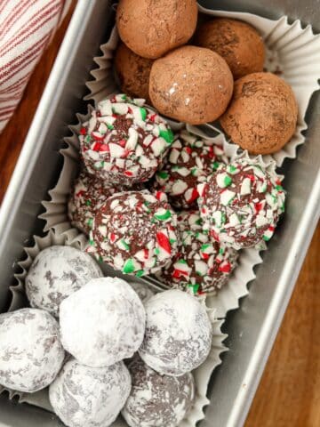 A loaf pan filled with three different types of truffles: one with cocoa, one with powdered sugar, and one with crushed candy canes.