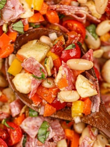 A wooden spoon scooping a portion of bean salad with sun-dried tomatoes, mozzarella, and basil.