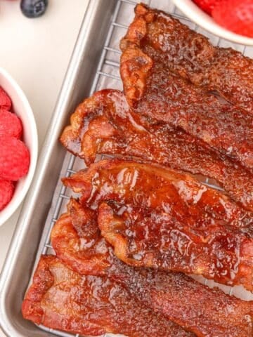 A stack of glazed bacon slices piled on top of a wire rack.