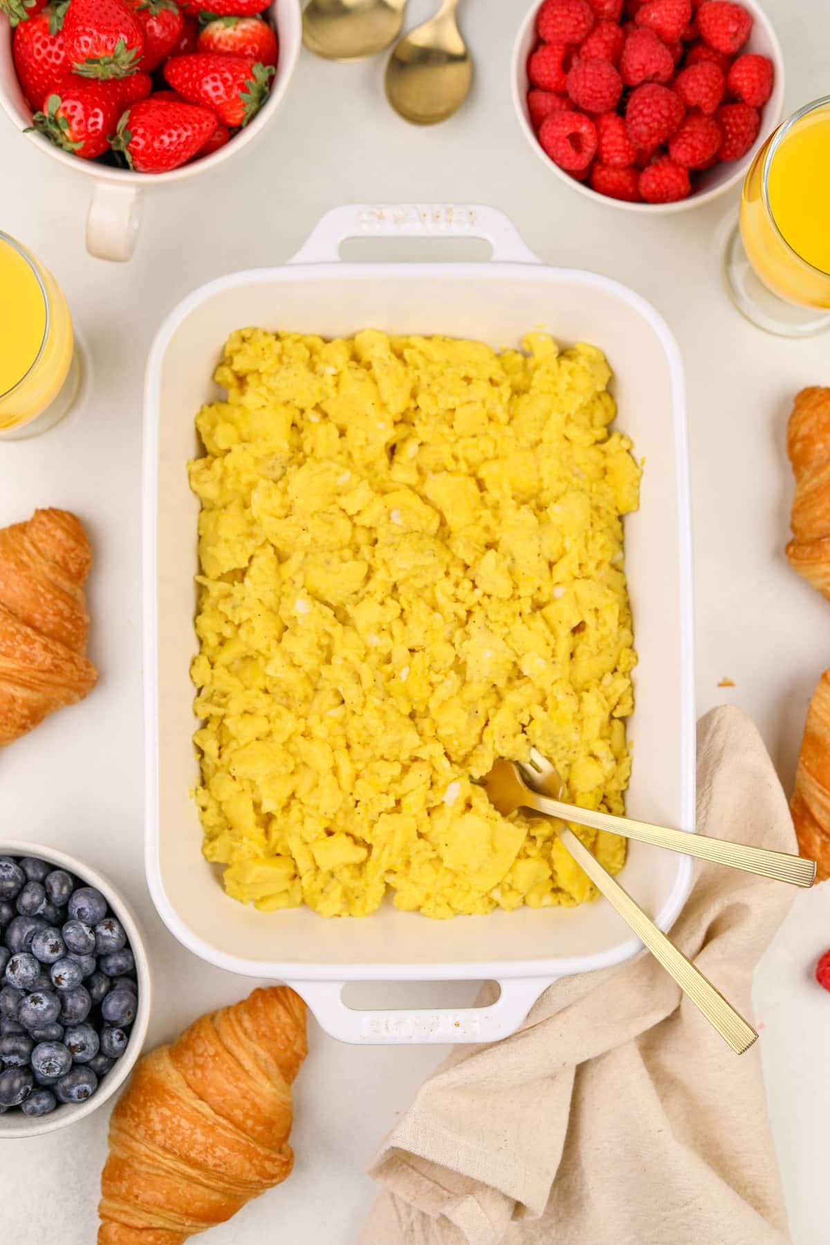 A white baking dish filled with cooked eggs, surrounded by fresh berries.