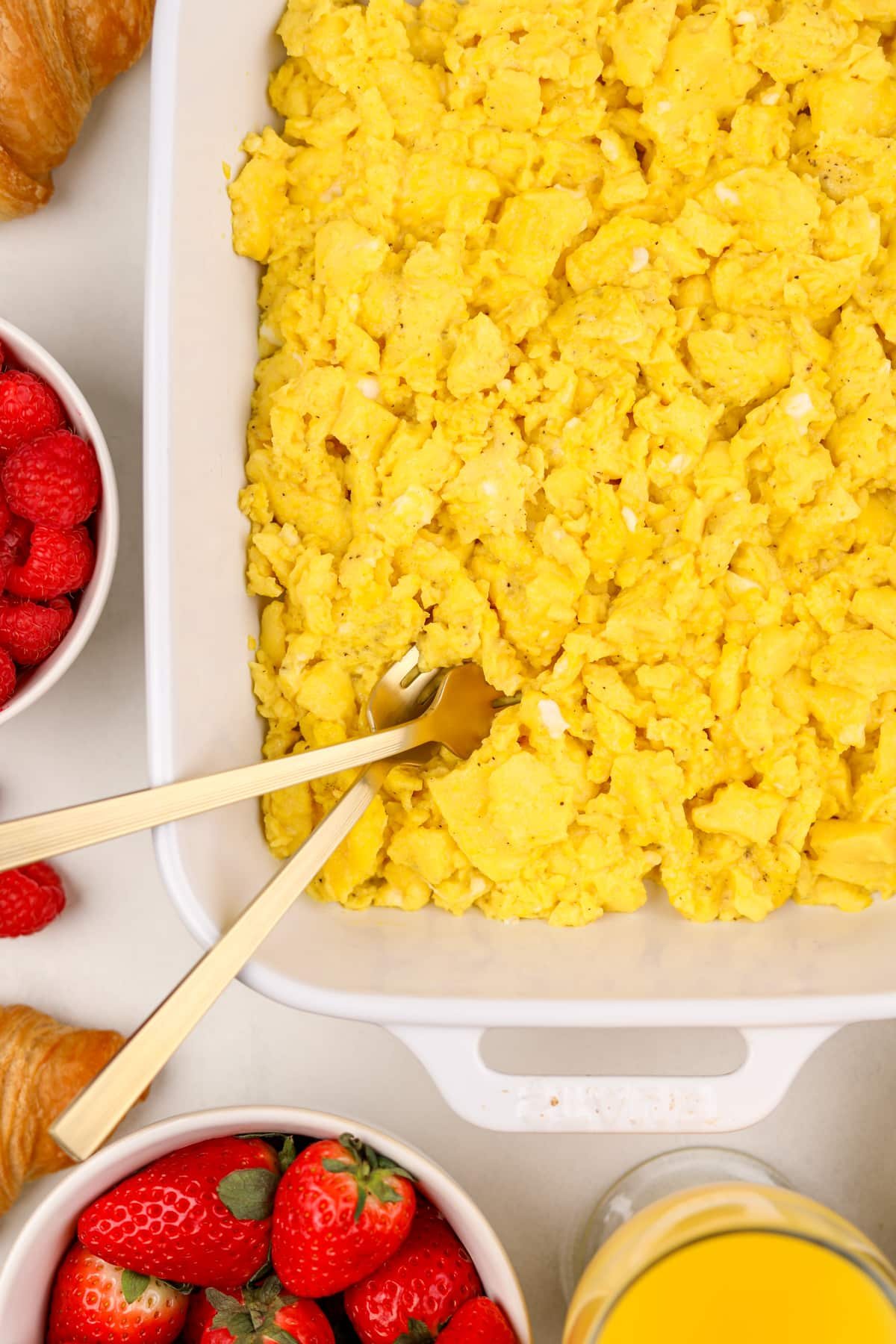 A close up of a baking dish with scrambled eggs and two gold forks fluffing them.