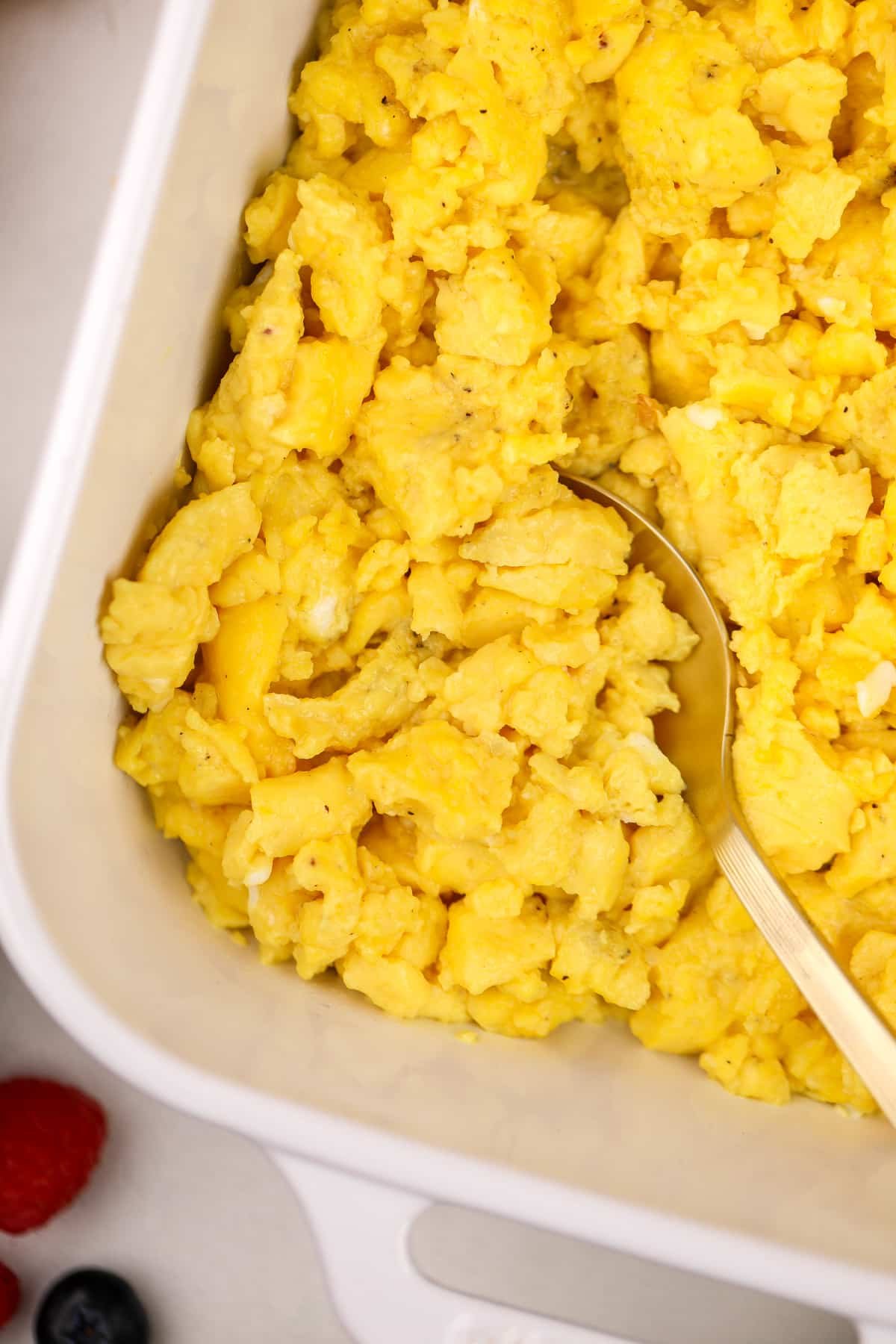 Scooping scrambled eggs from a baking dish.