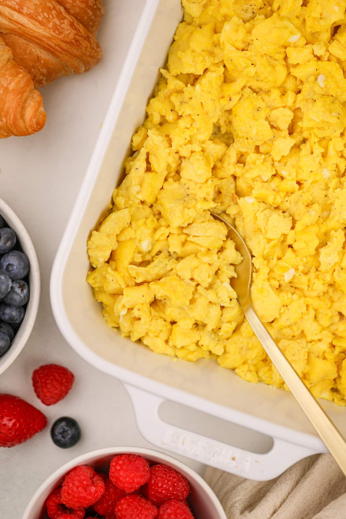 A gold spoon scooping scrambled eggs from a baking dish.