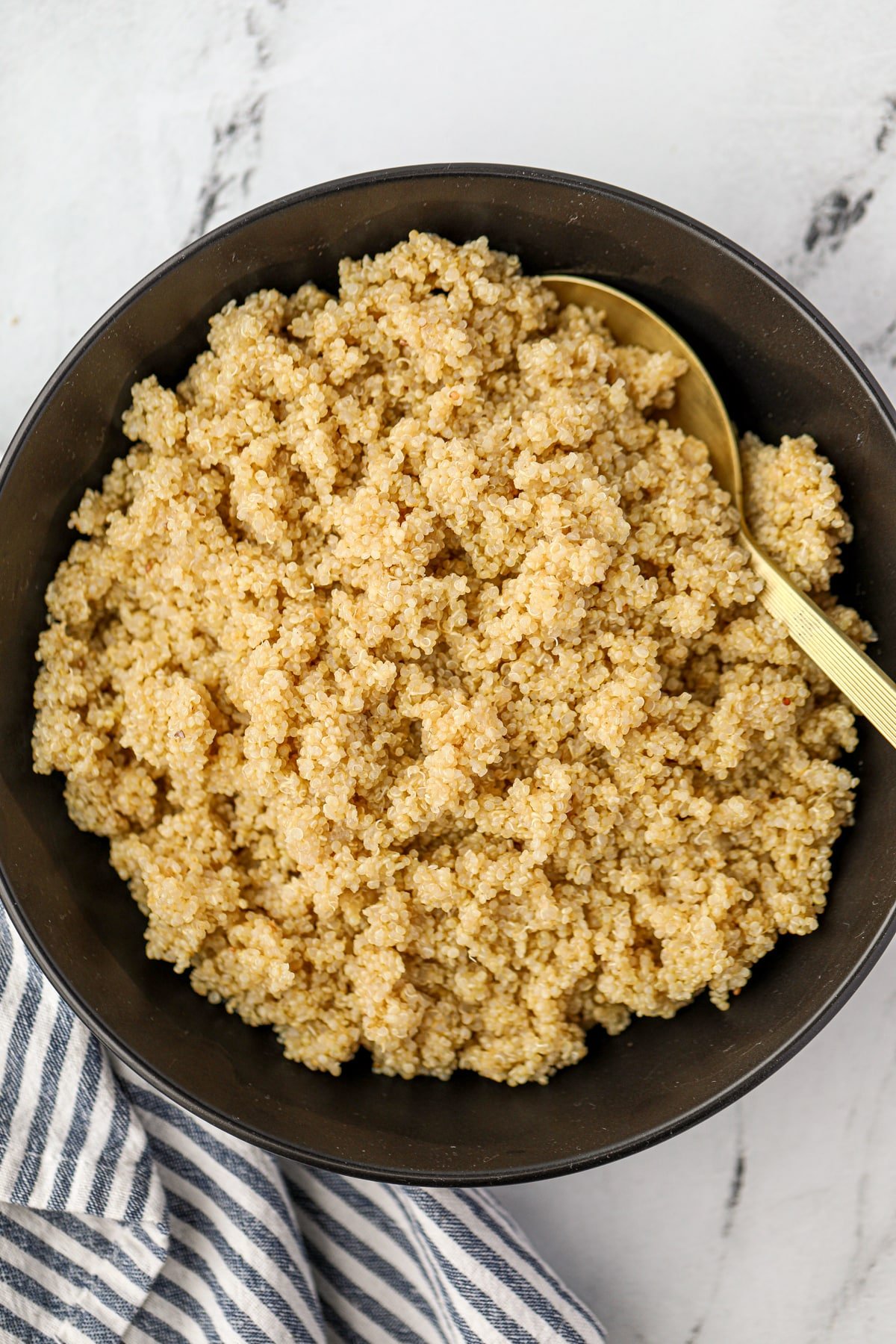 A golden spoon scooping quinoa from a black bowl.