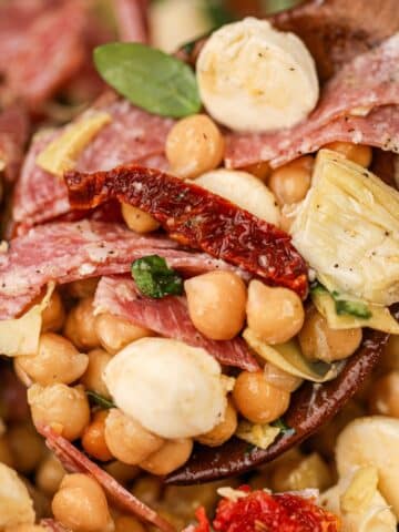 A wooden spoon scooping bean salad made with mozzarella, sun-dried tomato, and basil.