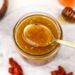 A small jar filled with homemade vinaigrette, a golden spoon taking a small amount.