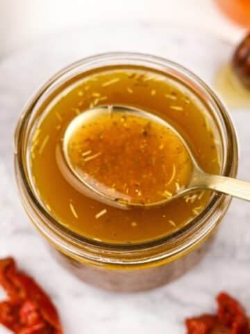 A small jar filled with homemade vinaigrette, a golden spoon taking a small amount.