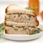 A stack of tuna sandwich halves on a white plate, garnished with fresh dill.