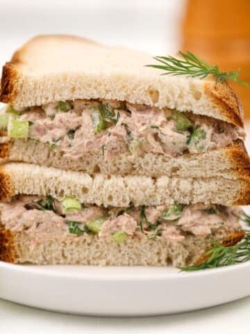 A stack of tuna sandwich halves on a white plate, garnished with fresh dill.