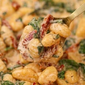 A close up of gnocchi in a creamy sauce, dotted with sundried tomato and spinach.