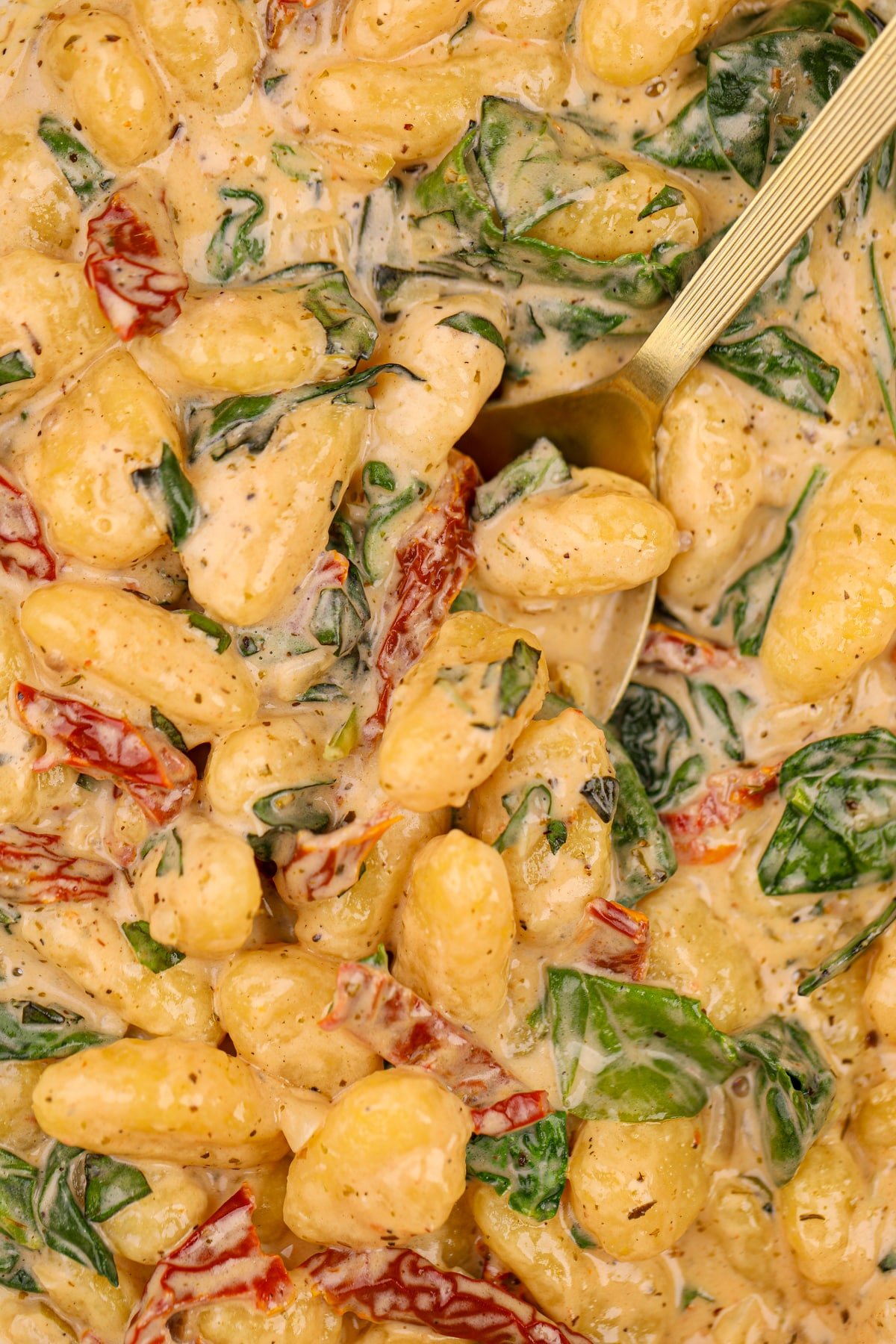 A large spoon taking a portion of creamy gnocchi from a pan.