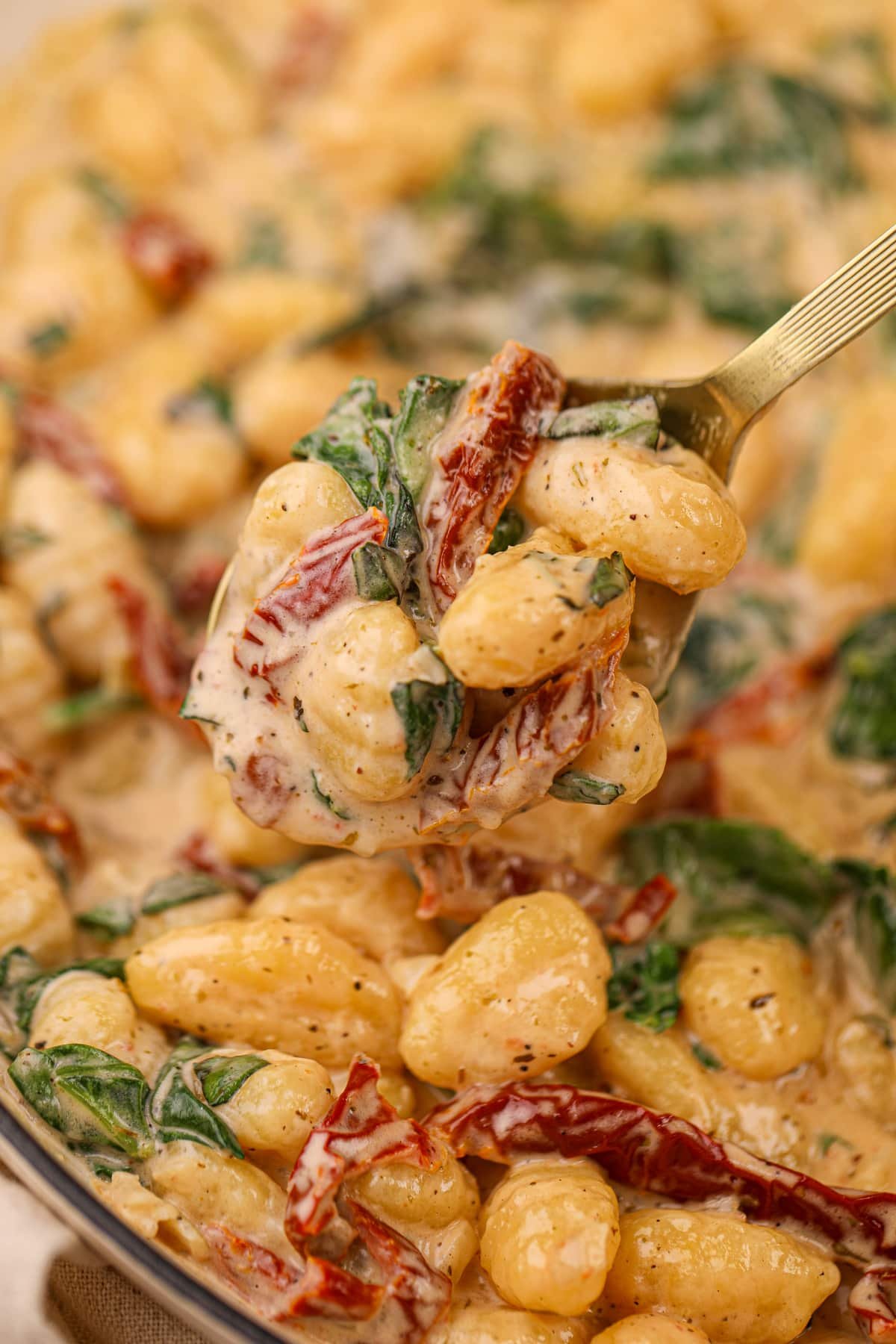 A spoon taking a portion of creamy gnocchi from a large pile.