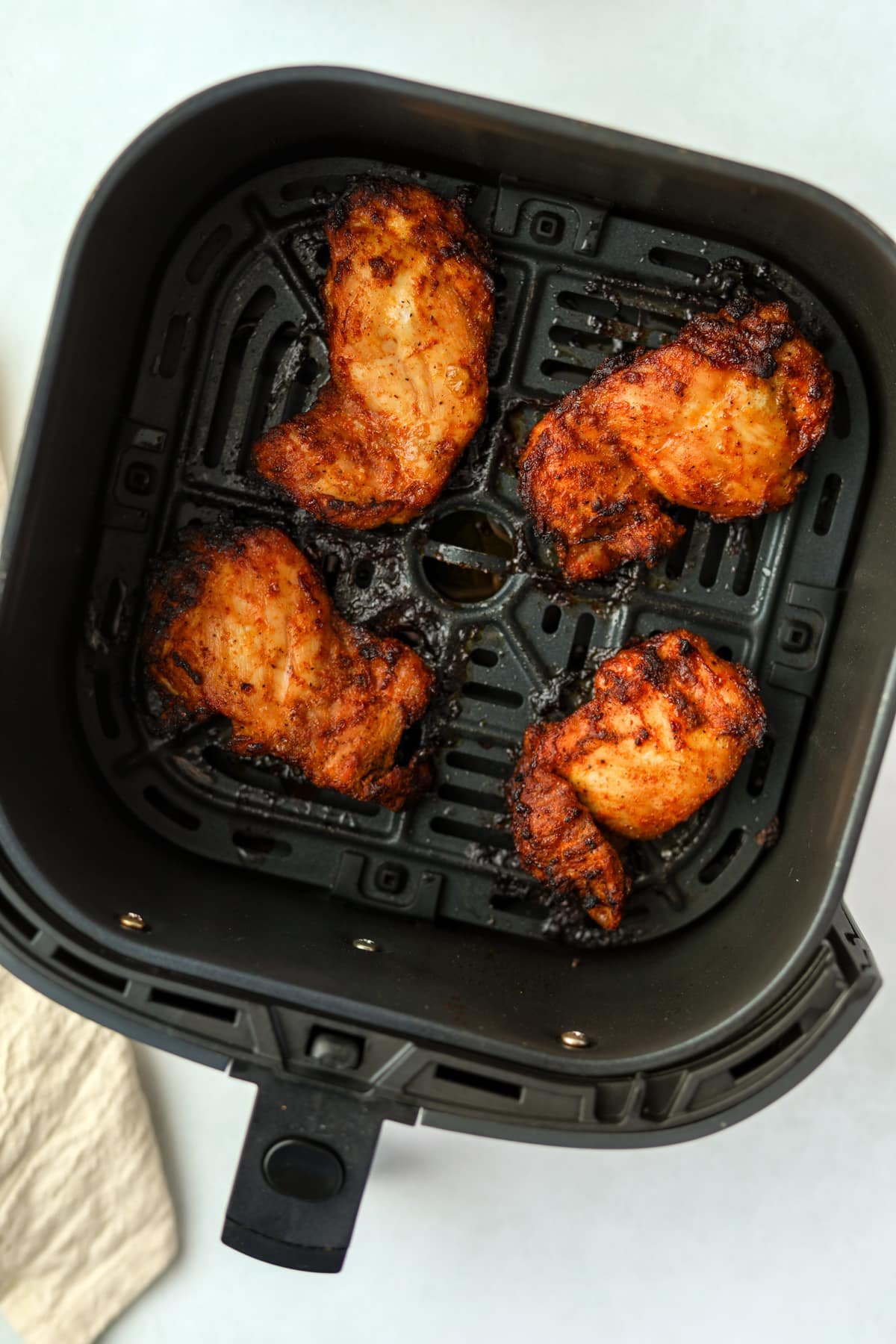 An air fryer basket with cooked chicken thigh pieces.