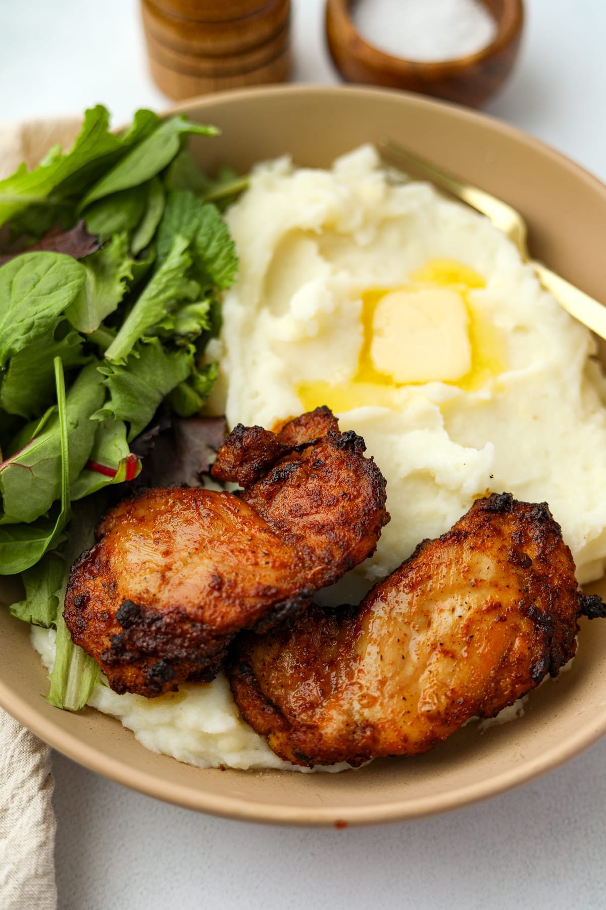 A close up of two cooked chicken thighs on a bed of mashed potatoes.