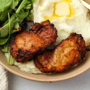 Two crisp chicken thighs on a bed of mashed potatoes.