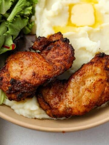 Two crisp chicken thighs on a bed of mashed potatoes.