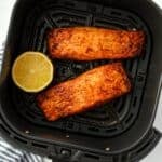 Two cooked salmon fillets in a black air fryer basket.