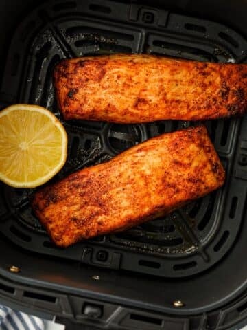 Two cooked salmon fillets in a black air fryer basket.