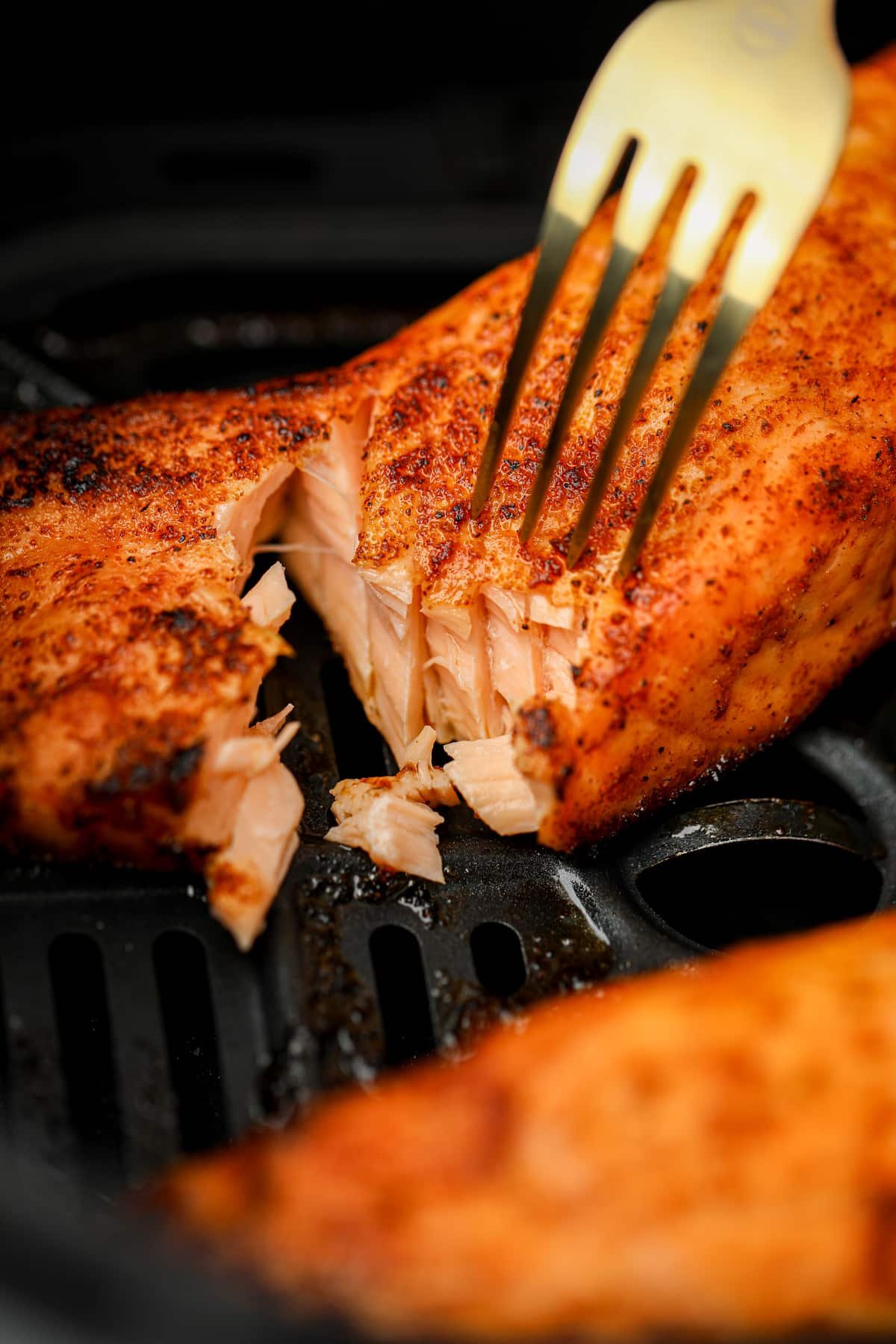 A fork that has flaked a piece of cooked salmon to expose the juicy insides.