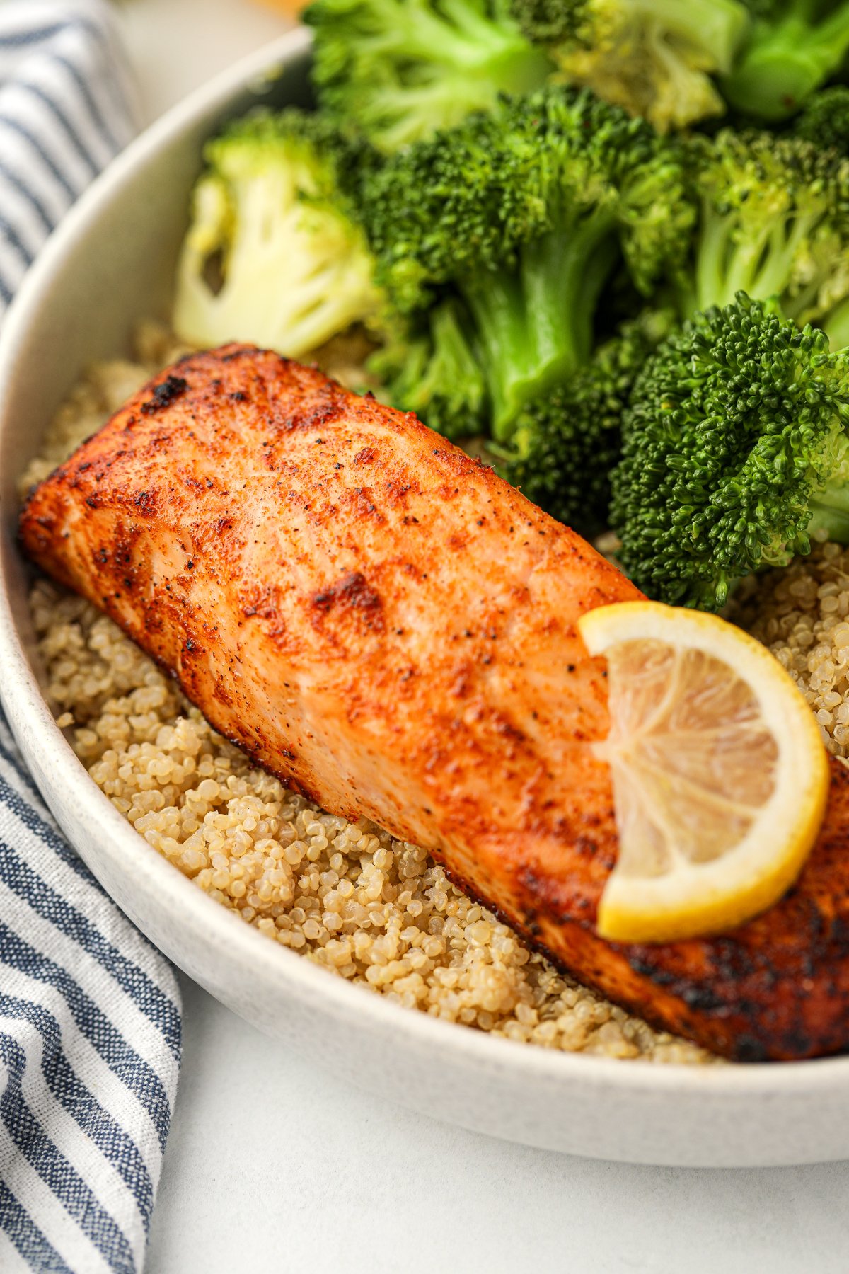 A close up of a fillet of salmon on a bed of quinoa and surrounded by broccoli.
