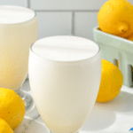 A glass of frosted lemonade with lemons in the background.