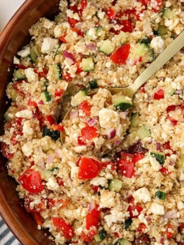 A spoon scooping a portion of Greek quinoa salad from a large wooden bowl.