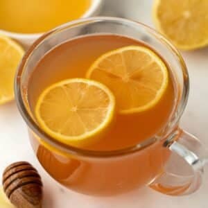 A glass mug filled with orange hued tea and garnished with lemon slices.