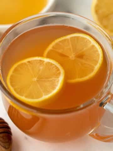 A glass mug filled with orange hued tea and garnished with lemon slices.