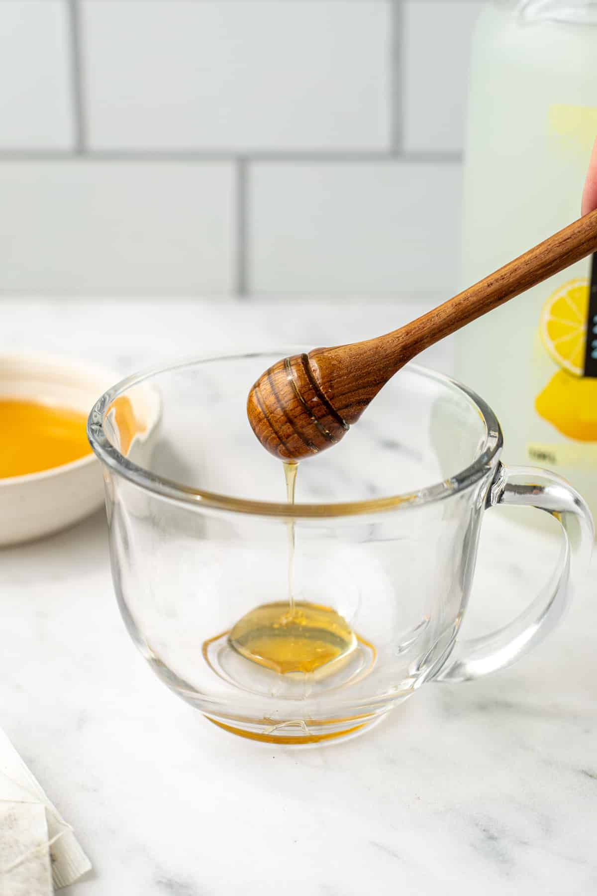 Drizzling honey into a glass mug.