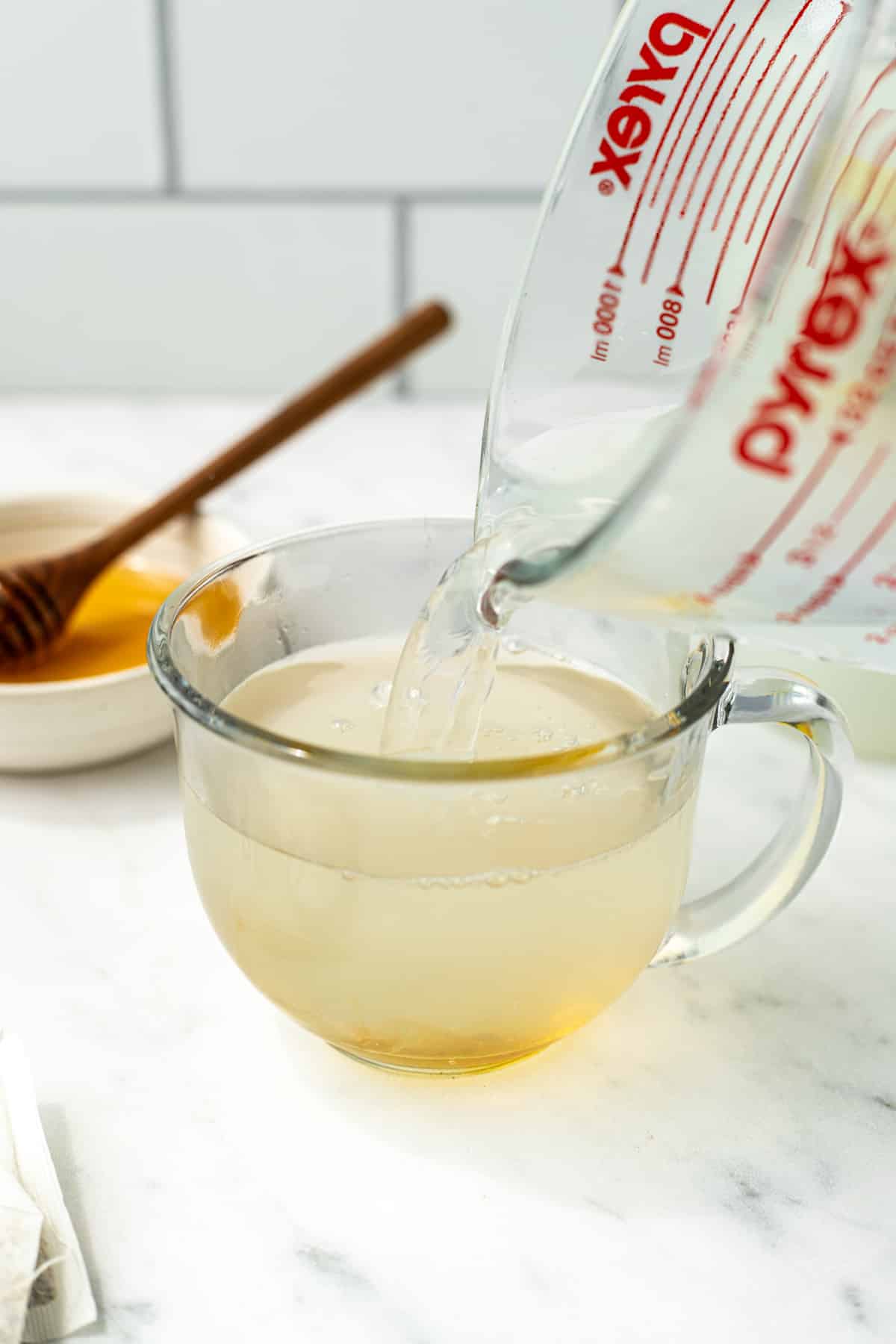 Pouring hot liquid into a glass mug with honey at the bottom.