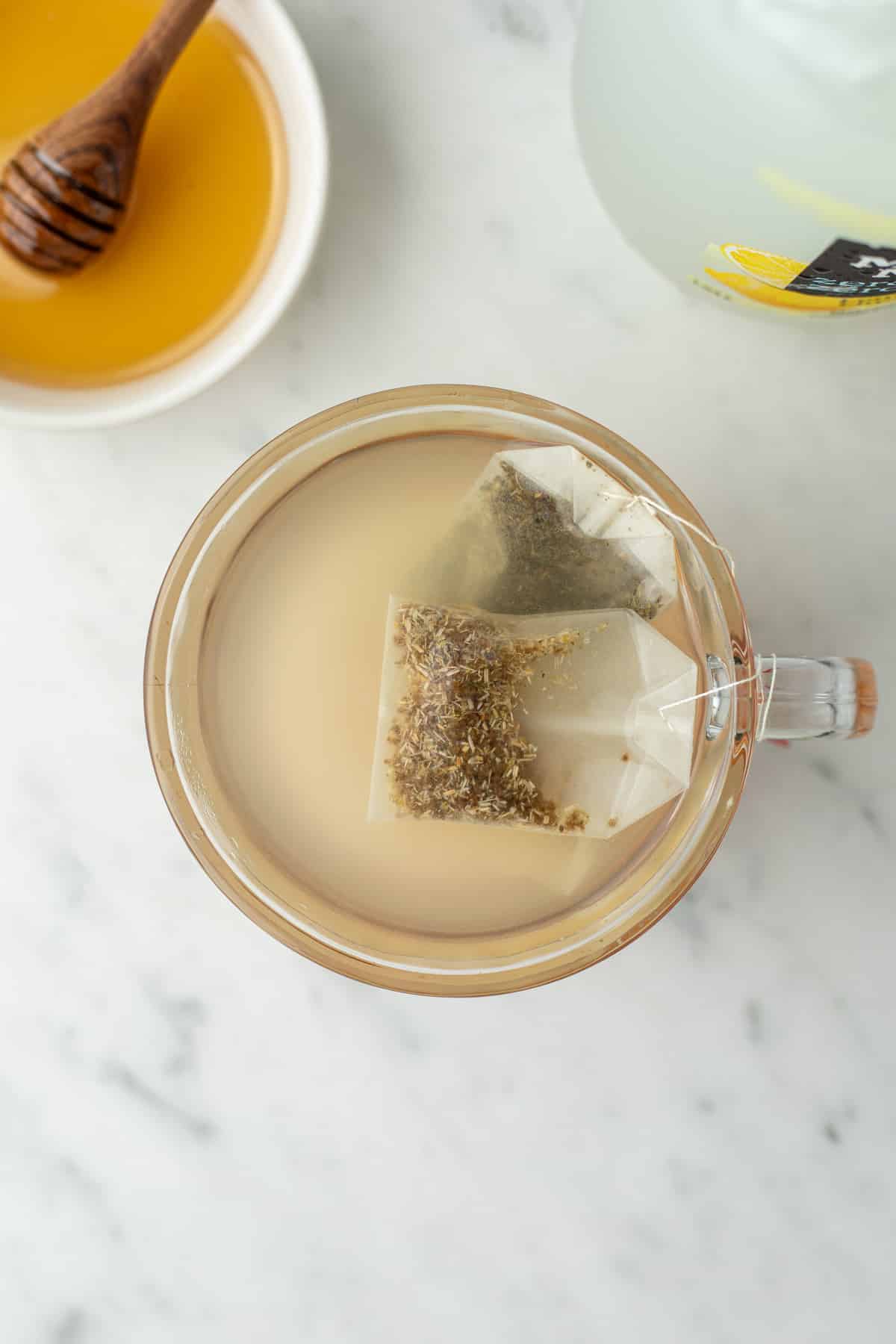 3 tea bags in a glass mug of warm liquid.