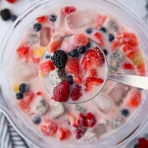 A bowl of fruit and milky liquid, with a ladle taking a portion from the middle.