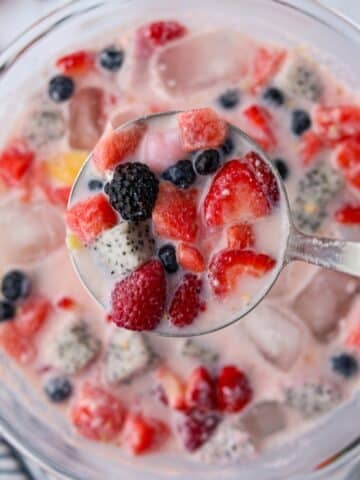 A bowl of fruit and milky liquid, with a ladle taking a portion from the middle.