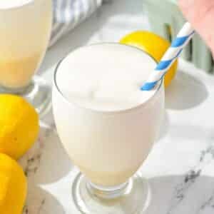 A small glass filled with frosted lemonade with a straw being placed on the side.