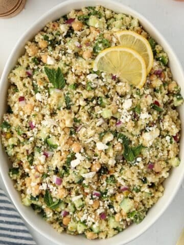 A large bowl of quinoa salad garnished with lemon and feta.