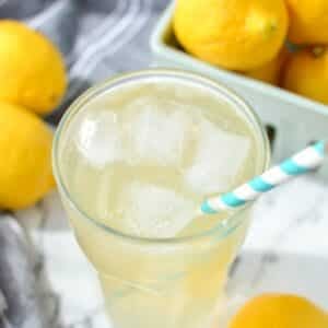 A glass of lemonade wiht a paper straw inserted into the glass.