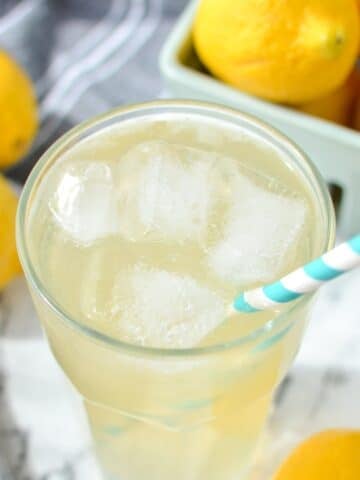 A glass of lemonade wiht a paper straw inserted into the glass.