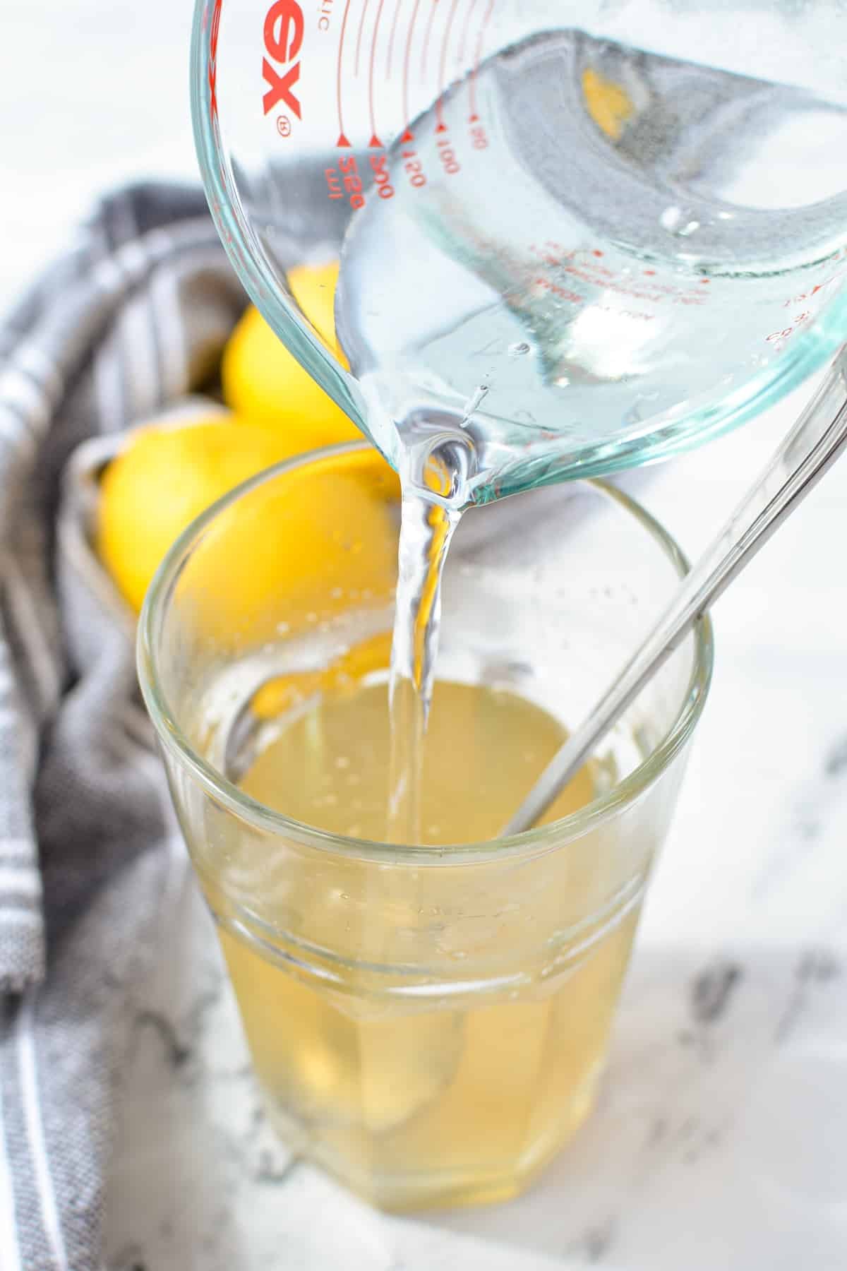 Pouring water into a glass with liquid in it.