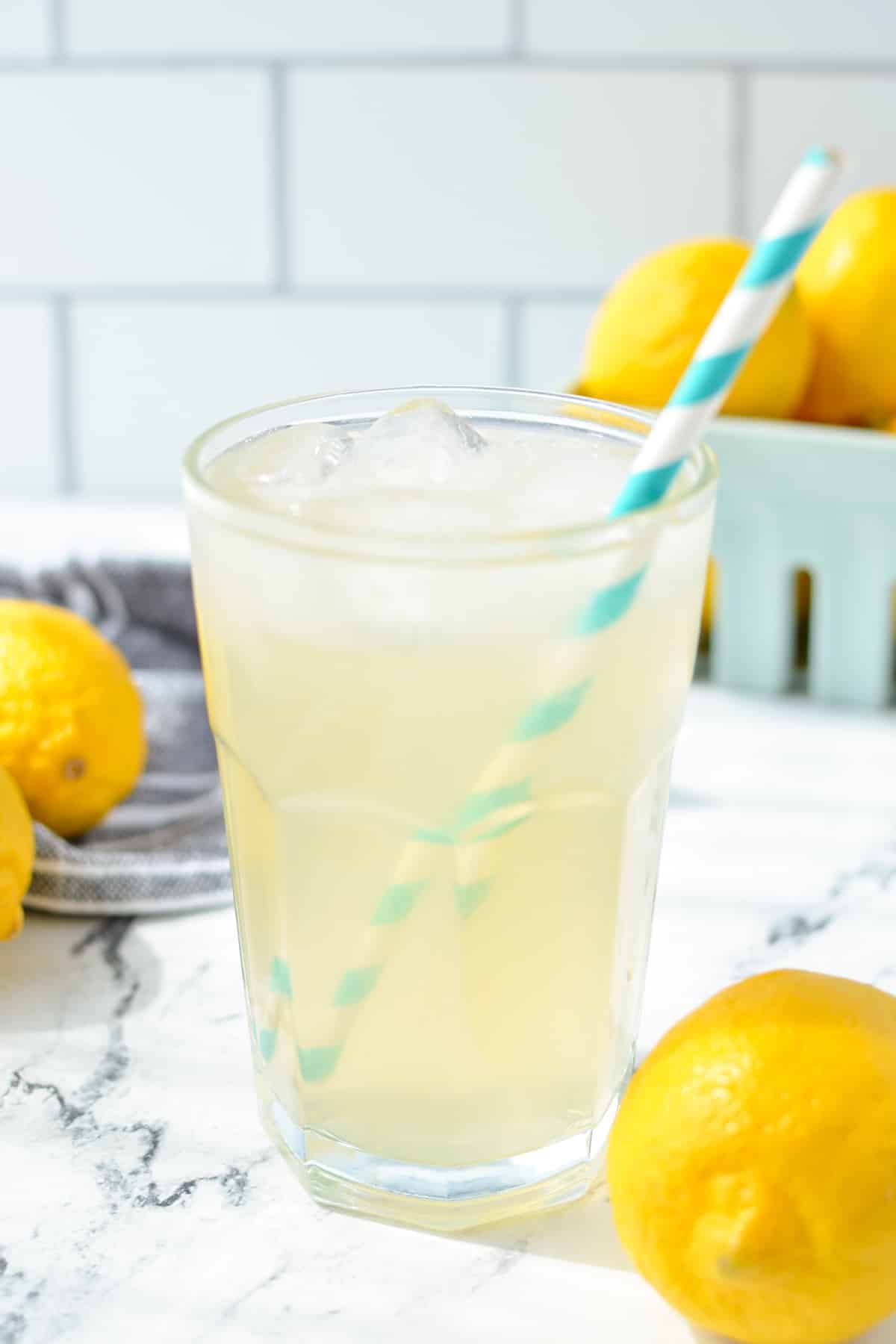 A glass of lemonade with a paper straw with lemons in the background.