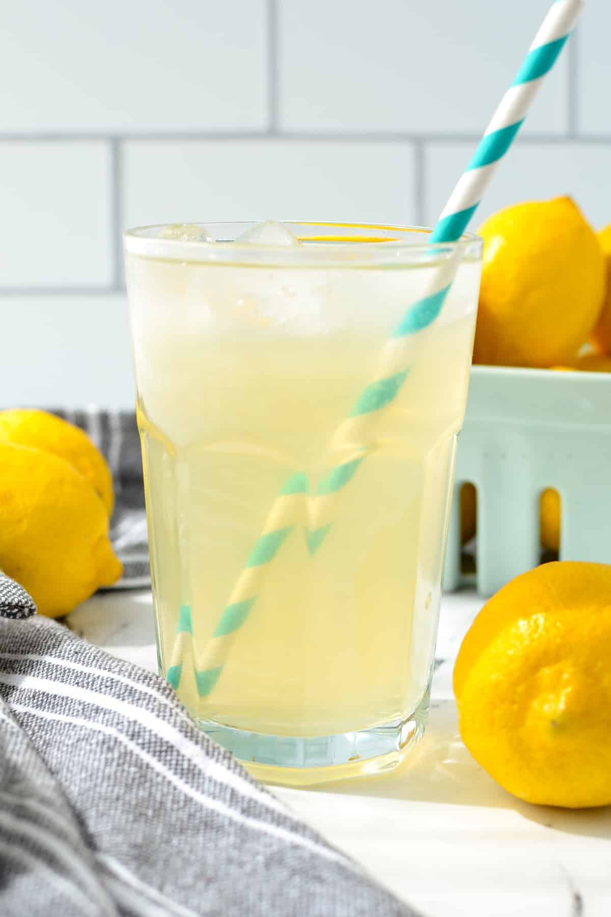 A glass of lemonade with multiple fresh lemons in the background. 