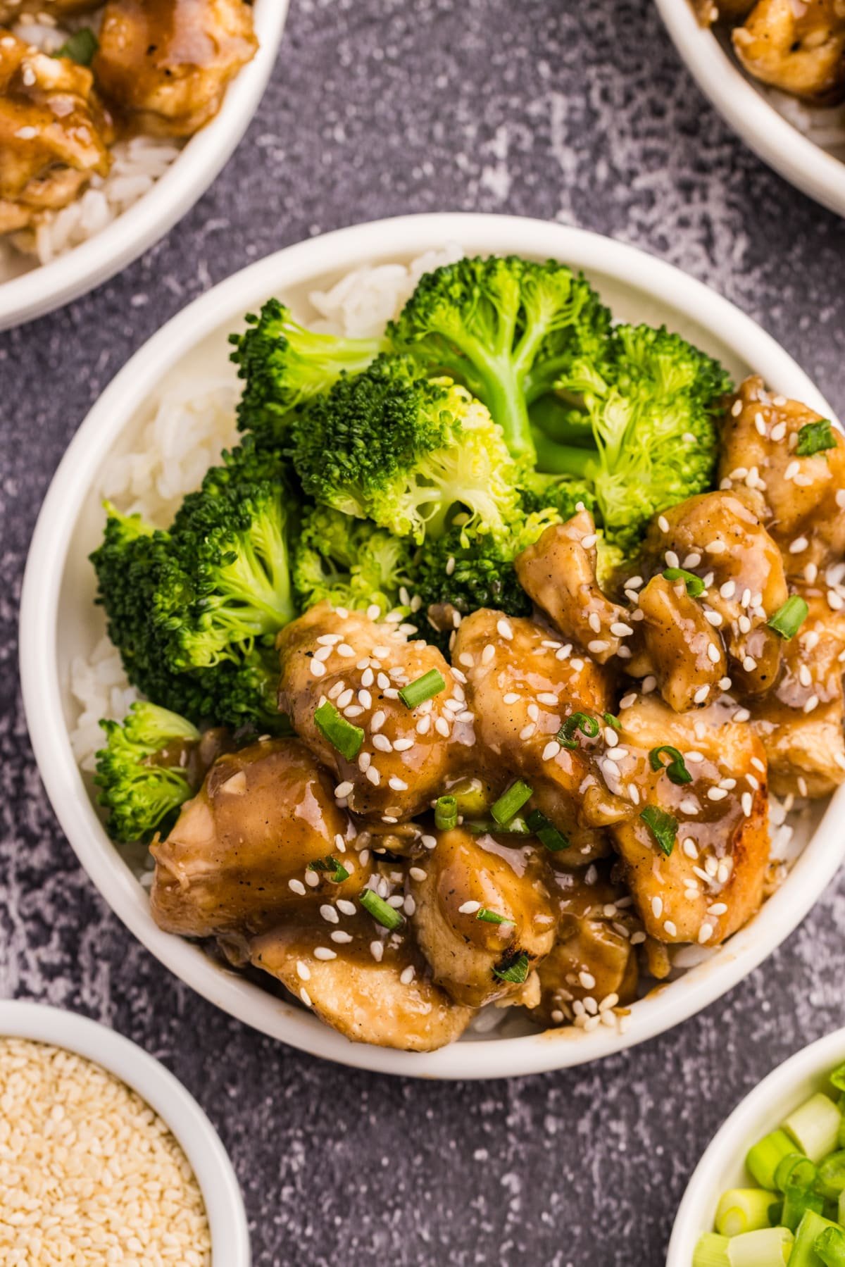 A bowl of rice topped with cooked chicken in sauce and steamed broccoli.