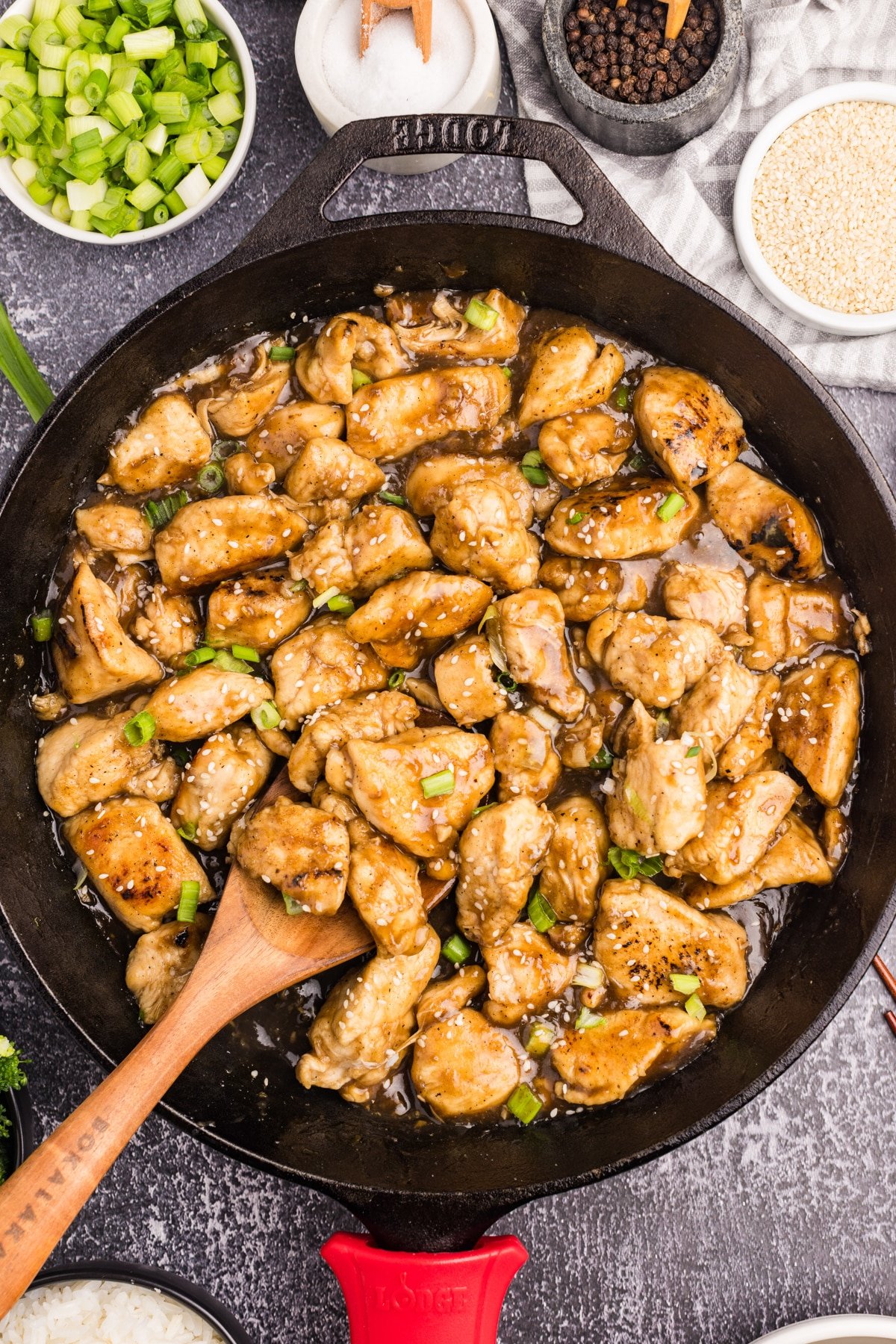 A cast iron skillet filled with chicken stir fry, being scooped with a wooden spoon.