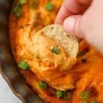 Dipping a tortilla chip into a bright orange chicken dip.