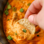 Dipping a round tortilla chip into creamy buffalo chicken dip.