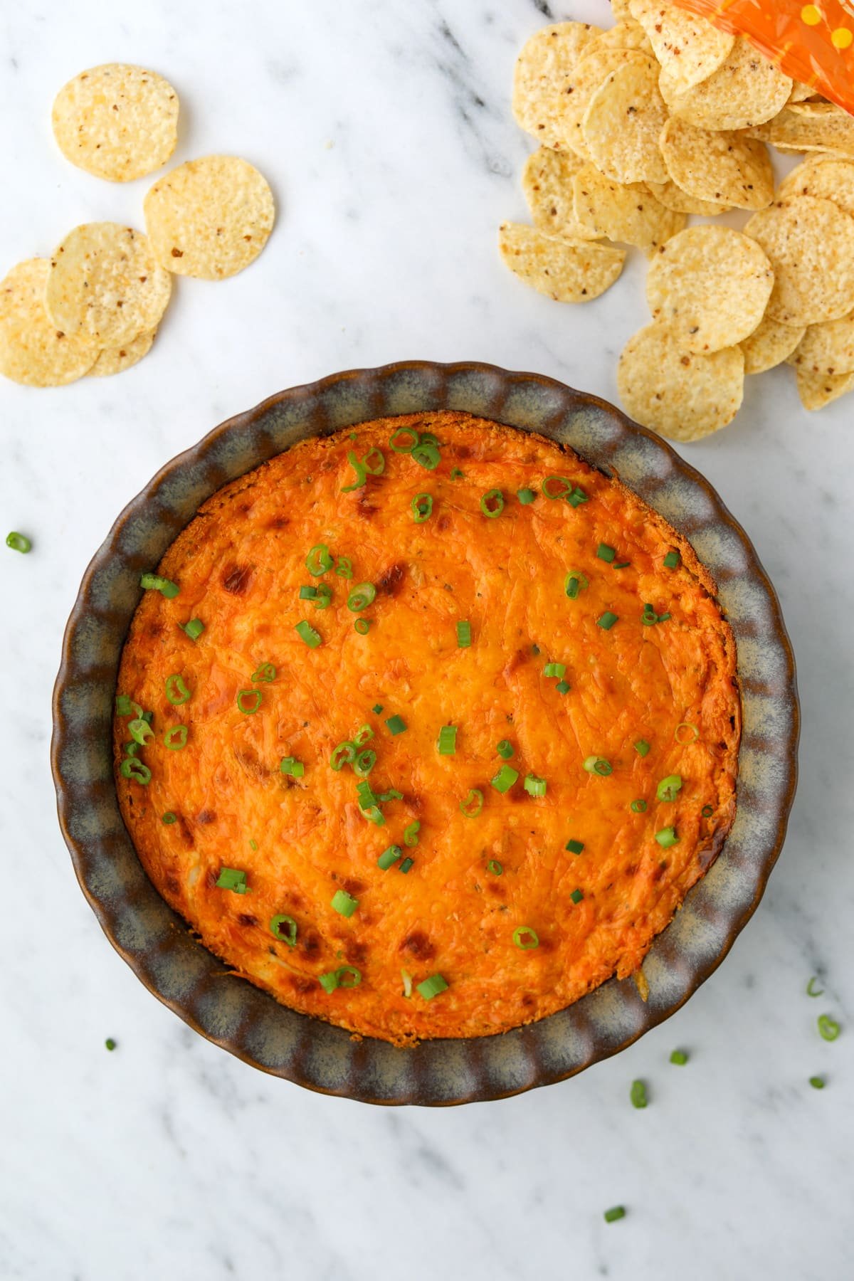 A brightly colored buffalo chicken dip in a pie plate, surrounded by tortilla chips.