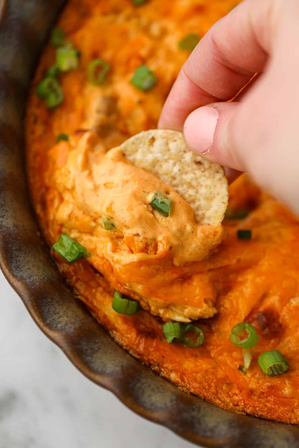 Dipping a tortilla chip into a cheesy buffalo dip.